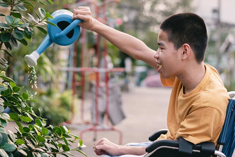 Disabled boy in sitting in a wheelchair and watering flowers.