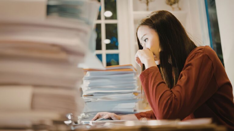 image of a person working at a desks with stack of work to do